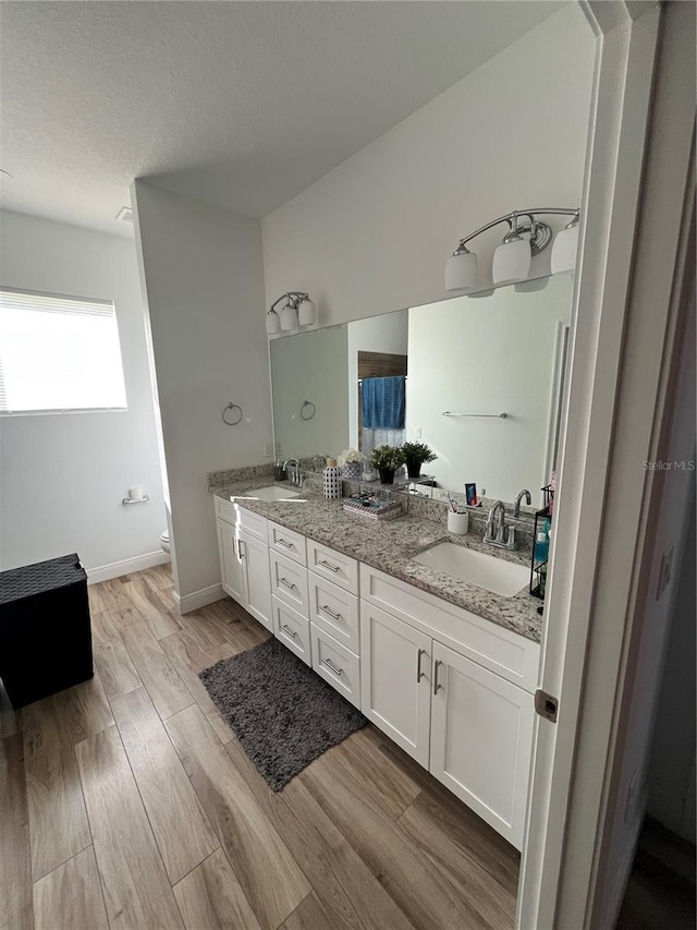 full bathroom with double vanity, toilet, a sink, and wood finished floors