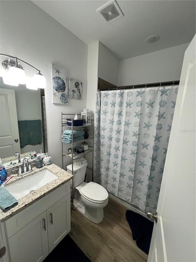 full bath featuring visible vents, toilet, wood finished floors, a textured ceiling, and vanity