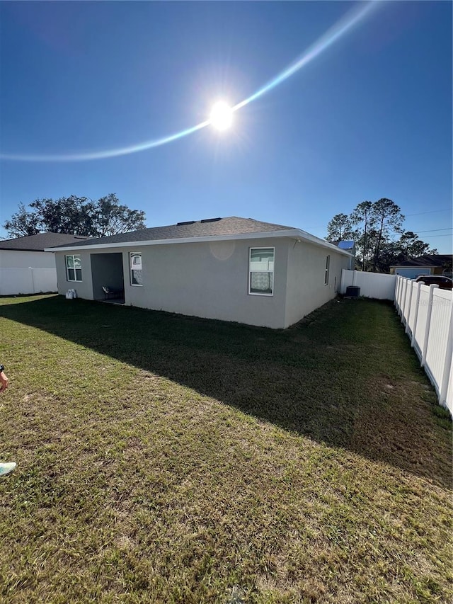 rear view of property with a fenced backyard, a yard, and stucco siding