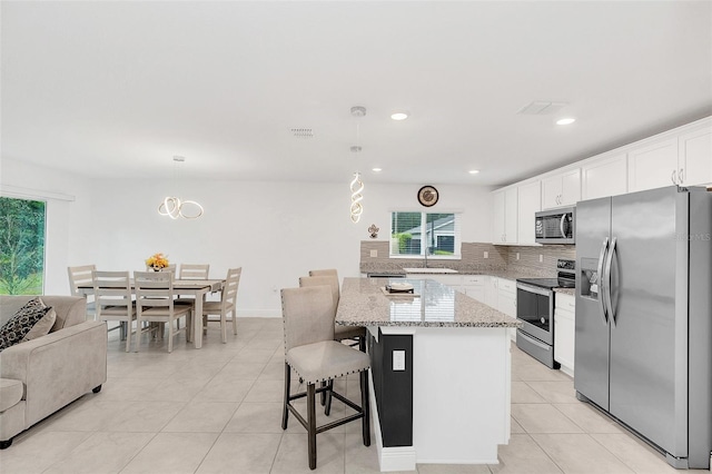 kitchen with stainless steel appliances, a kitchen island, white cabinetry, open floor plan, and decorative light fixtures