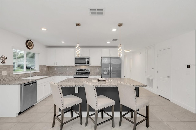 kitchen featuring stainless steel appliances, a kitchen island, a sink, visible vents, and hanging light fixtures