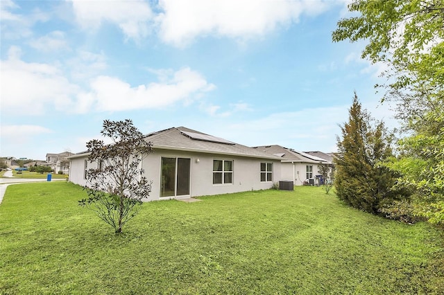 back of property with cooling unit, solar panels, a lawn, and stucco siding