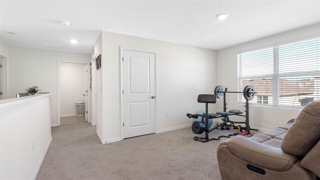 workout area with light carpet, baseboards, and a textured ceiling