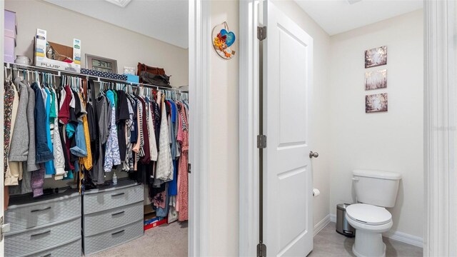 interior space with a walk in closet, toilet, and baseboards