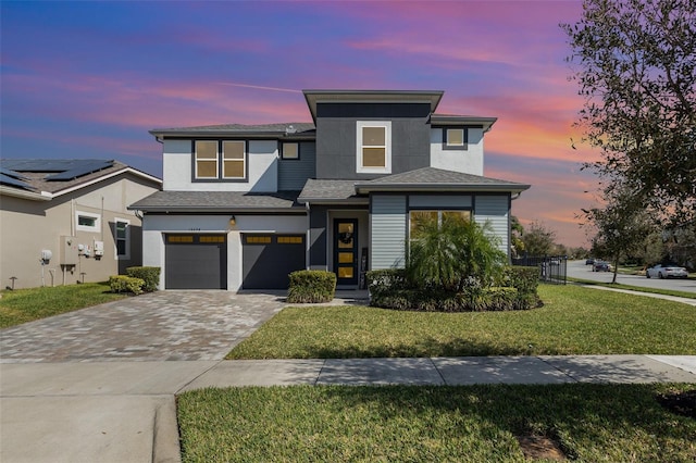 view of front facade featuring an attached garage, a lawn, and decorative driveway