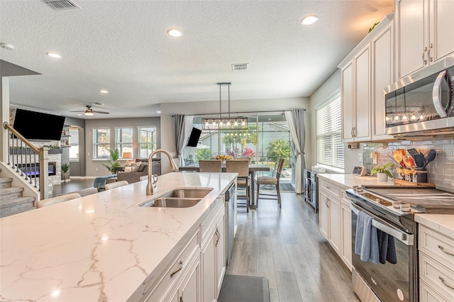 kitchen with appliances with stainless steel finishes, open floor plan, hanging light fixtures, white cabinetry, and a sink