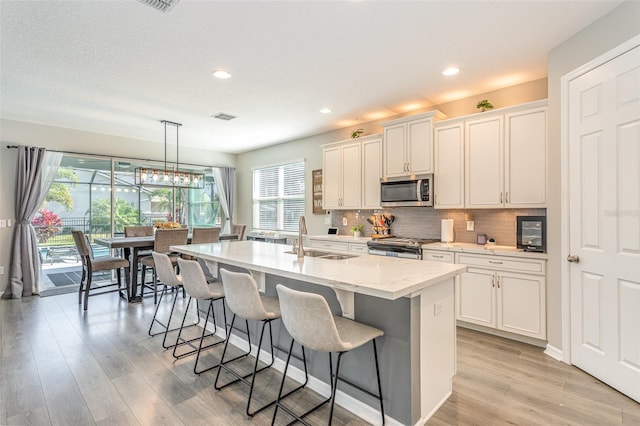 kitchen featuring a center island with sink, appliances with stainless steel finishes, hanging light fixtures, white cabinetry, and a sink