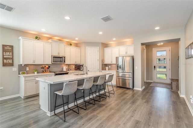 kitchen featuring stainless steel appliances, a kitchen island with sink, white cabinets, and visible vents