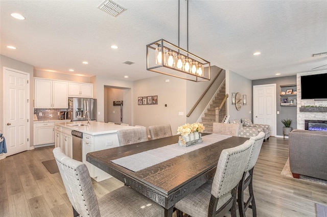 dining room with stairs, a stone fireplace, a textured ceiling, and light wood-style flooring