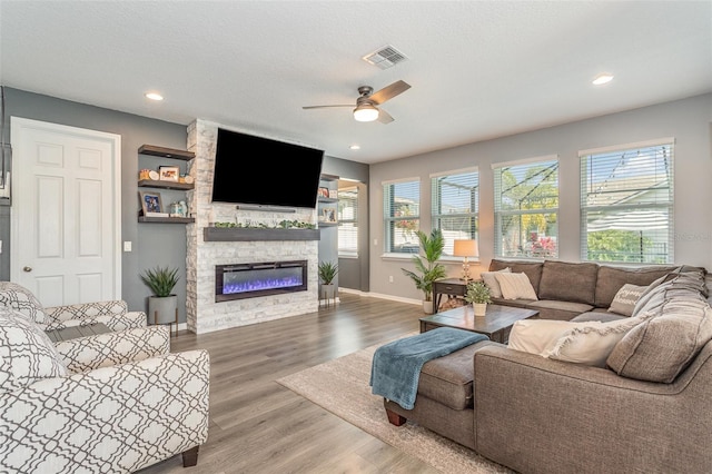 living area with a stone fireplace, visible vents, a wealth of natural light, and wood finished floors