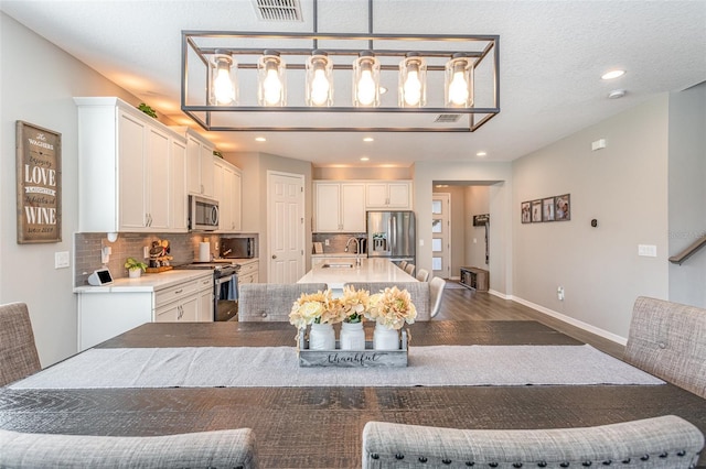 kitchen featuring tasteful backsplash, decorative light fixtures, stainless steel appliances, white cabinetry, and a sink