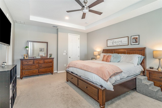 bedroom featuring a tray ceiling, visible vents, light carpet, ceiling fan, and baseboards