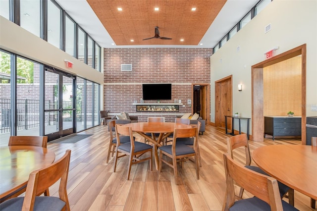 dining room with ceiling fan, brick wall, a towering ceiling, and light wood-style floors