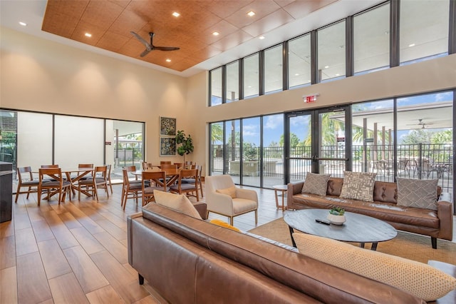 living area featuring ceiling fan, light wood finished floors, plenty of natural light, and a towering ceiling