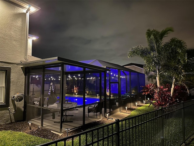 patio at night with glass enclosure, fence, and a fenced in pool