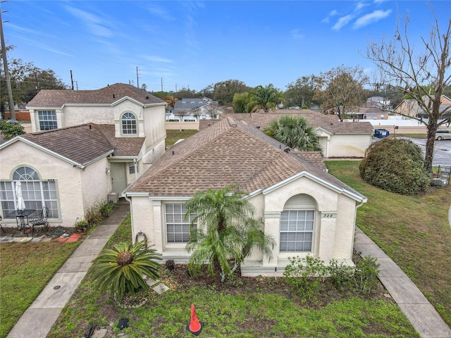 mediterranean / spanish-style home with a shingled roof, a front lawn, and stucco siding