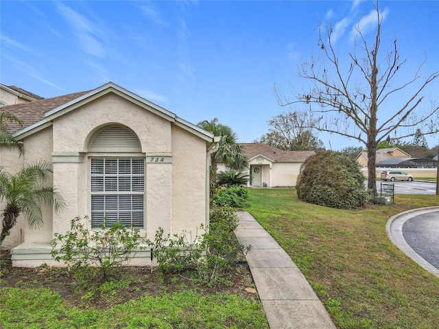 view of side of home with roof with shingles, a lawn, and stucco siding