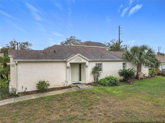 view of front of property with a shingled roof, a front yard, and stucco siding