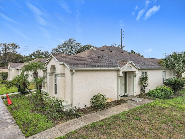 single story home with a front yard, roof with shingles, and stucco siding