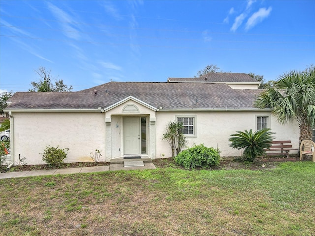 view of front of property with a shingled roof, a front lawn, and stucco siding