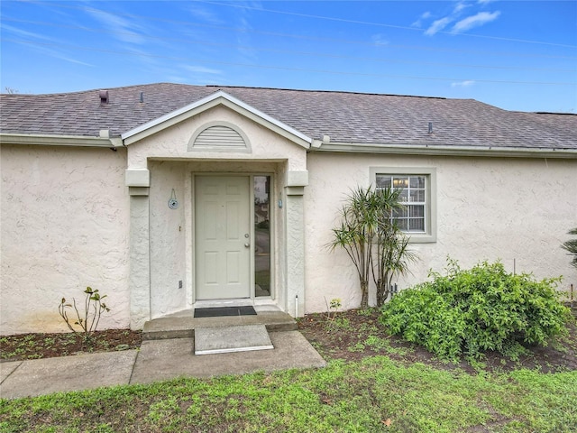 doorway to property featuring roof with shingles and stucco siding