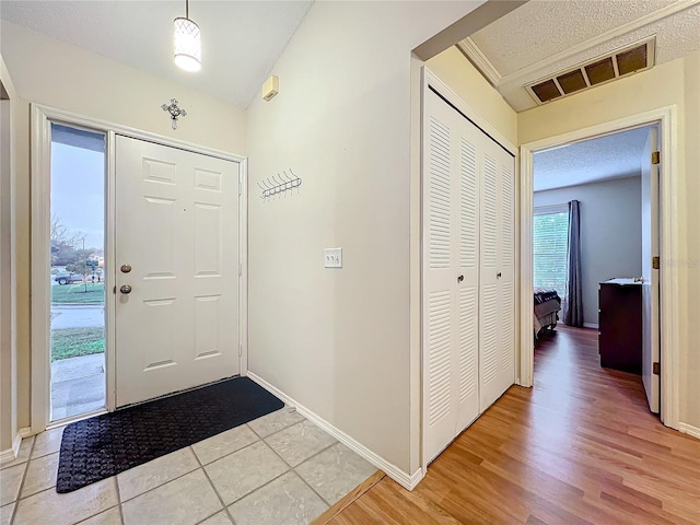 foyer entrance featuring lofted ceiling, visible vents, light wood-style floors, a textured ceiling, and baseboards