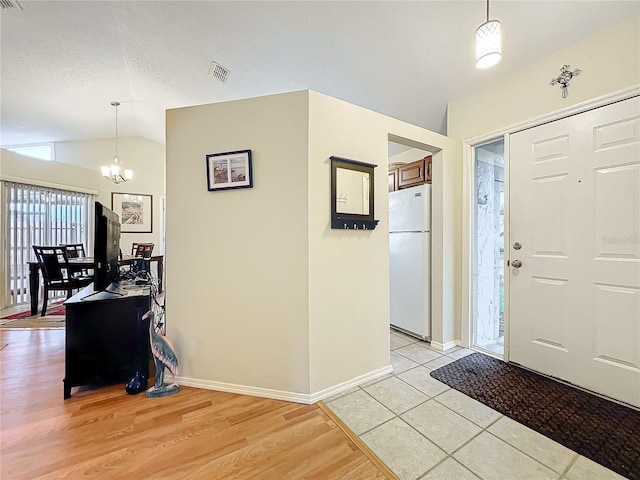 entrance foyer featuring lofted ceiling, visible vents, light wood-style flooring, a chandelier, and baseboards