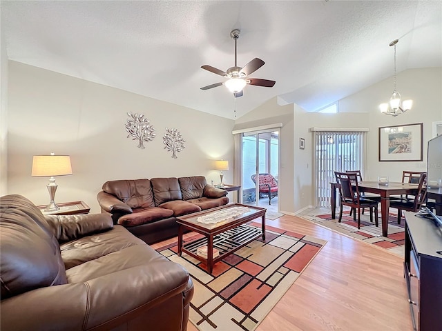 living area featuring lofted ceiling, light wood-style floors, a textured ceiling, baseboards, and ceiling fan with notable chandelier