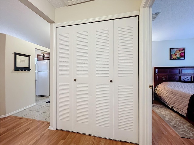 hallway featuring visible vents, light wood-style flooring, baseboards, and a textured ceiling