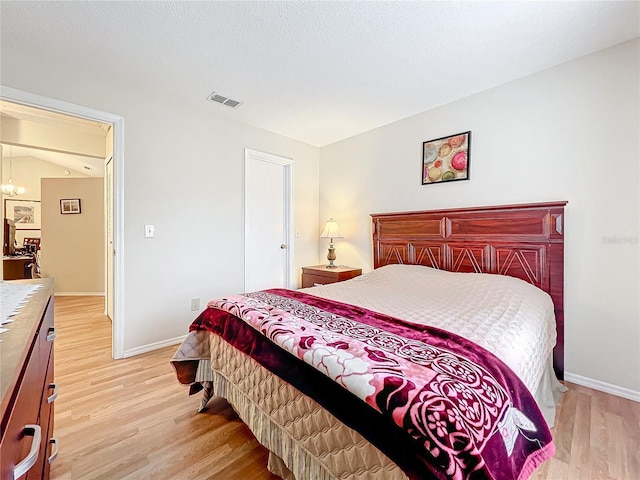 bedroom featuring light wood finished floors, an inviting chandelier, visible vents, and baseboards