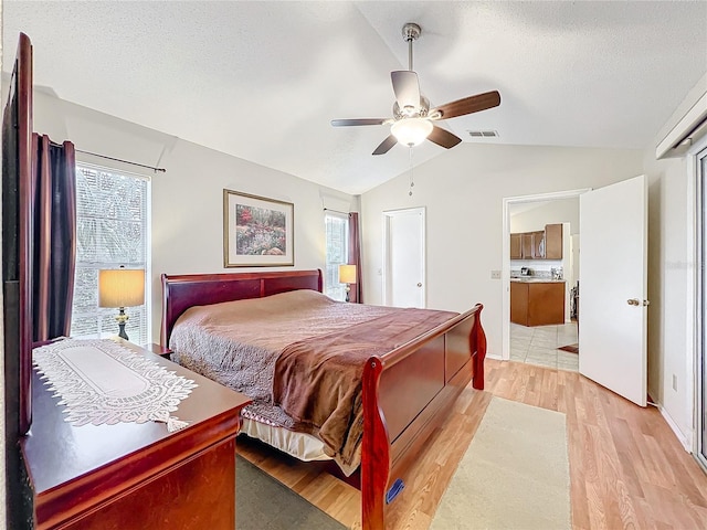 bedroom with lofted ceiling, light wood finished floors, visible vents, and a textured ceiling