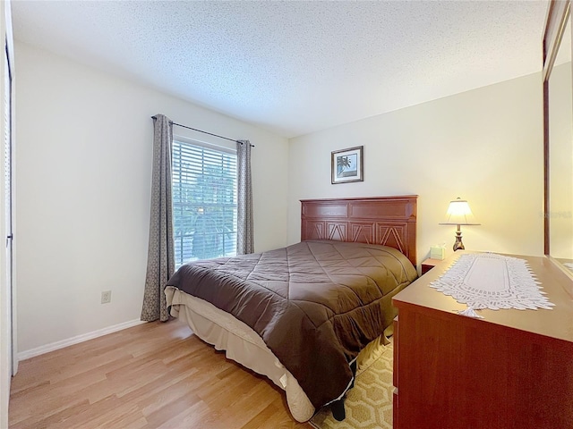 bedroom featuring light wood-type flooring, baseboards, and a textured ceiling