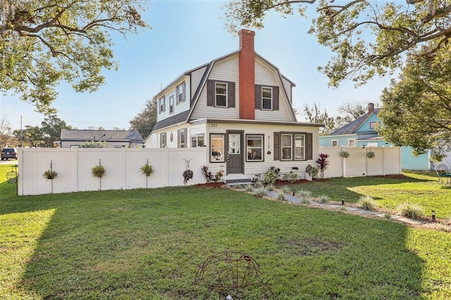 rear view of property featuring a lawn, fence, and a gambrel roof