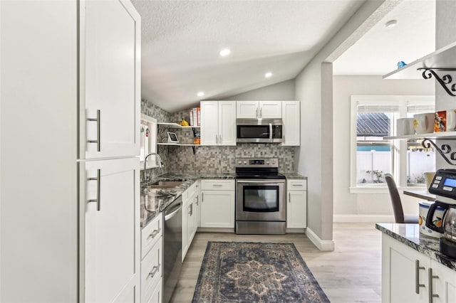 kitchen with open shelves, stainless steel appliances, lofted ceiling, a sink, and dark stone countertops