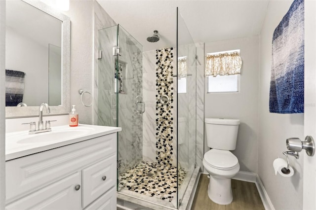 bathroom with toilet, a shower stall, vanity, wood finished floors, and baseboards