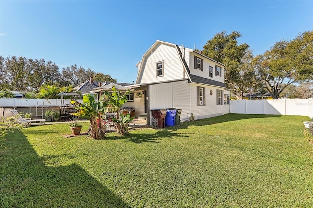 rear view of property featuring a fenced backyard, a lawn, and a gambrel roof