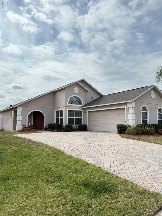 ranch-style home with a front lawn, decorative driveway, an attached garage, and stucco siding