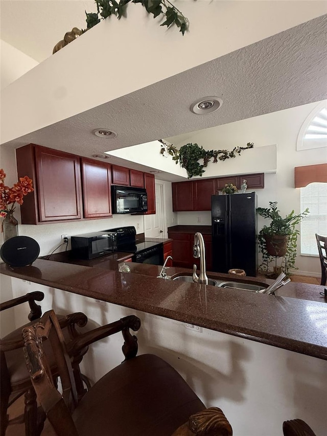 kitchen with a textured ceiling, black appliances, dark countertops, and reddish brown cabinets