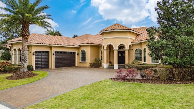 mediterranean / spanish-style home featuring decorative driveway, stucco siding, a garage, a tiled roof, and a front lawn