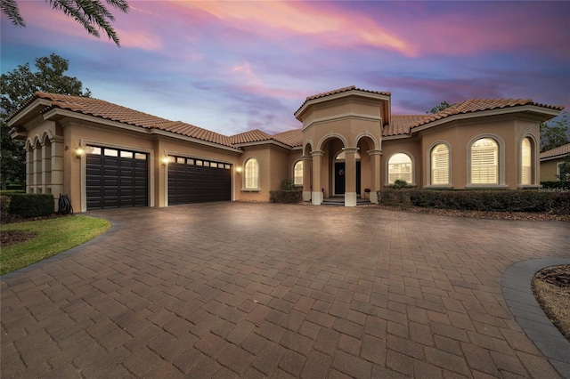 mediterranean / spanish-style home with a garage, a tiled roof, decorative driveway, and stucco siding