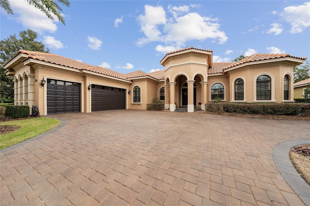 mediterranean / spanish home with an attached garage, a tiled roof, decorative driveway, and stucco siding