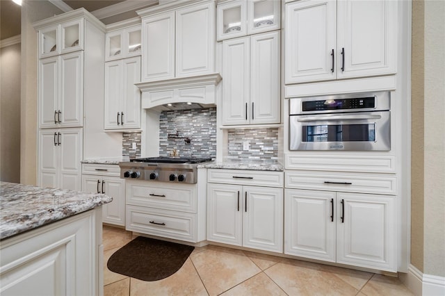 kitchen featuring light stone counters, stainless steel appliances, decorative backsplash, glass insert cabinets, and white cabinetry