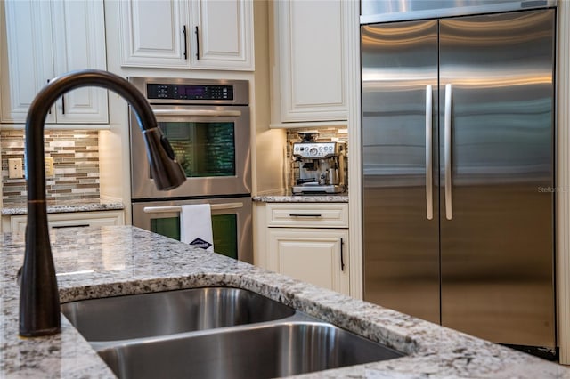 kitchen featuring appliances with stainless steel finishes, decorative backsplash, white cabinetry, and light stone countertops