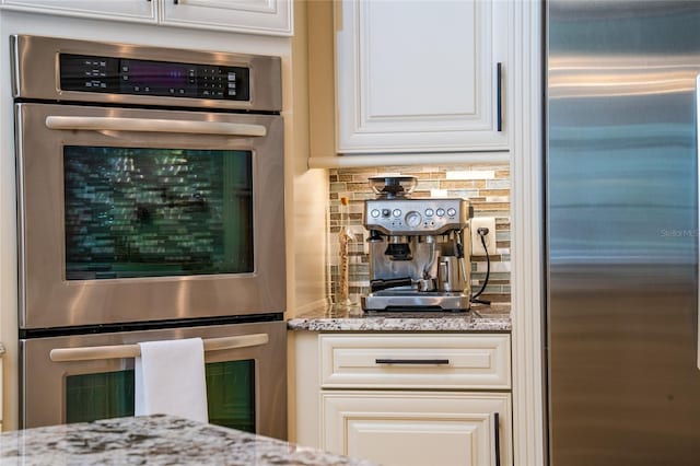 kitchen with tasteful backsplash, white cabinetry, light stone counters, and stainless steel appliances