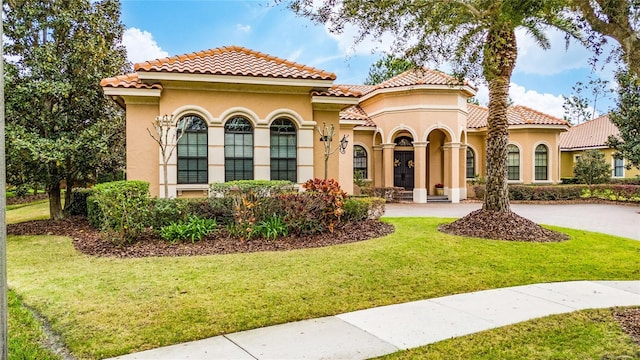 mediterranean / spanish-style home with a tiled roof, a front lawn, driveway, and stucco siding