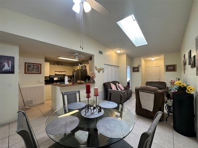 dining room with lofted ceiling with skylight, a ceiling fan, visible vents, and light tile patterned floors