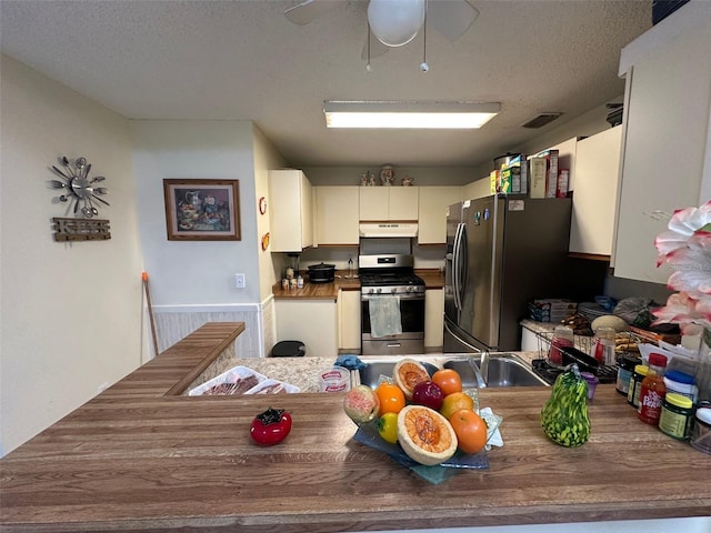 kitchen featuring stainless steel appliances, cream cabinetry, under cabinet range hood, and a textured ceiling