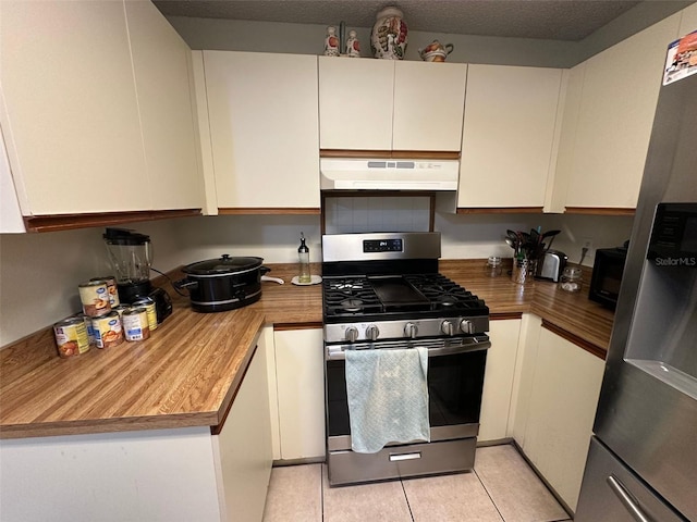 kitchen with a textured ceiling, light tile patterned flooring, under cabinet range hood, white cabinets, and appliances with stainless steel finishes