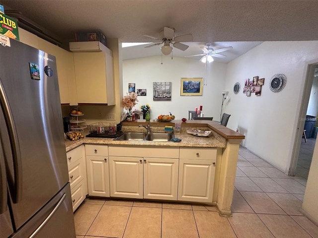 kitchen featuring light tile patterned floors, a peninsula, a sink, light countertops, and freestanding refrigerator