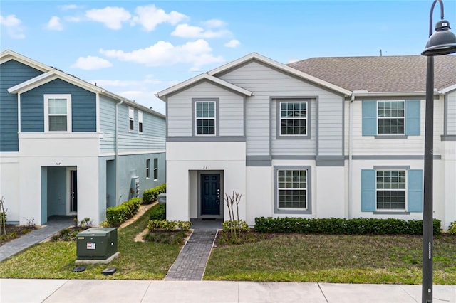 townhome / multi-family property featuring stucco siding, roof with shingles, and a front yard